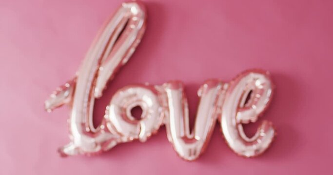 Rack focus video of shiny pale pink love text balloon, on pink background with copy space