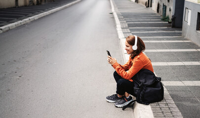 Fototapeta na wymiar Woman sitting on curbside listening to music using her headphones and mobile phone.