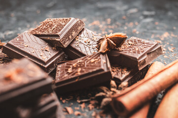 Dark chocolate bar pieces on dark background with grated chocolate and spices, pile chunks of broken chocolate