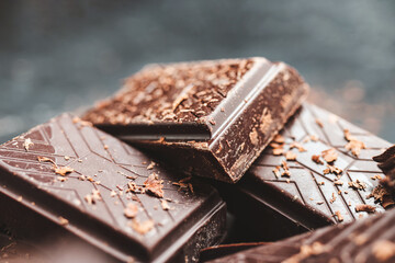 Dark chocolate bar pieces on dark background with grated chocolate and spices, pile chunks of broken chocolate