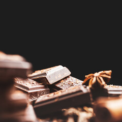 Dark chocolate bar pieces on dark background with copy-space, grated chocolate and spices, pile chunks of broken chocolate