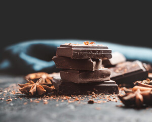 Dark chocolate bar pieces on dark background with copy-space, grated chocolate and spices, pile chunks of broken chocolate