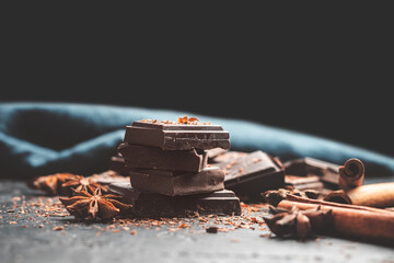 Dark chocolate bar pieces on dark background with copy-space, grated chocolate and spices, pile chunks of broken chocolate