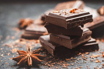 Dark chocolate bar pieces on dark background with grated chocolate and spices, pile chunks of broken chocolate