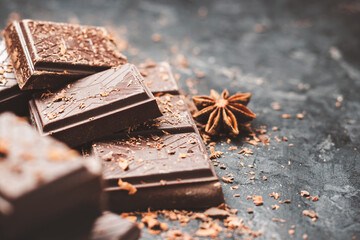 Dark chocolate bar pieces on dark background with grated chocolate and spices, pile chunks of...