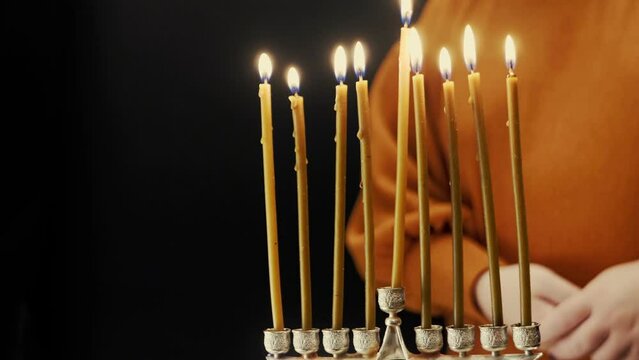 A woman's hand lights candles on the last day of Hanukkah from a shamash candle in a Hanukkah lamp