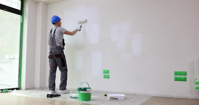 Builder in protective helmet and uniform overalls painting wall with roller 4k movie slow motion