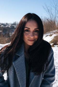 Portrait of a beautiful dark-haired girl with brown eyes on the street in snowy winter. Front view