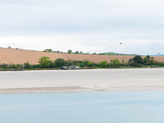 Seaside landscape and a farmer's field on a hill. Sandy seashore on a cloudy day. Calm water...