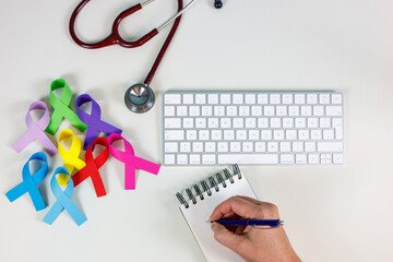 Woman doctor's hands writing on her desk next to a stethoscope and colorful ribbons, World cancer...