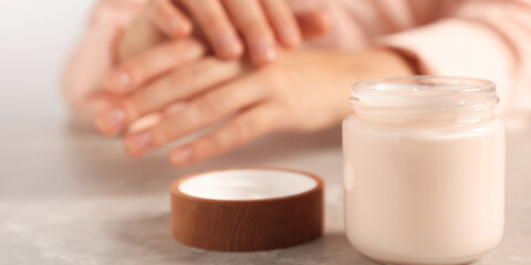 Obraz na płótnie Canvas Woman applying cosmetic cream onto hand at grey table, focus on jar. Banner design