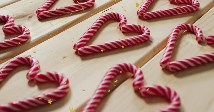 Animation of golden star icons over close up of candy cane on wooden surface