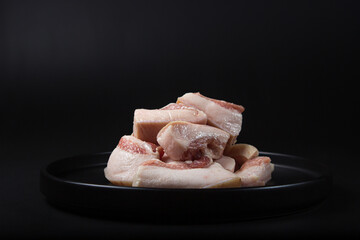 Sliced lard on a black plate on a black background. Fresh raw lard