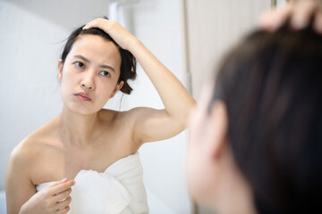 Fototapeta premium Problem skin. Concerned young asian women popping pimple on cheek while standing near mirror in bathroom. young asian women with acne