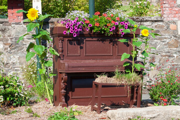 old piano in the street at sun with bench and flowers