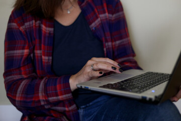 Unrecognizable cropped woman in plaid shirt using laptop on legs. Education at home, online school courses for student