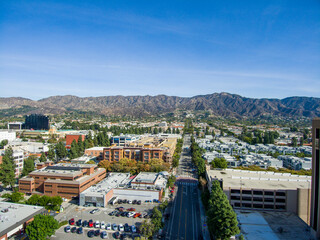 aerial shot of office buildings, apartments and shops surrounded by lush green trees, cars driving...