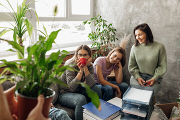 Smiling positive women choosing houseplants for new apartment, sit on sofa near table with paper...