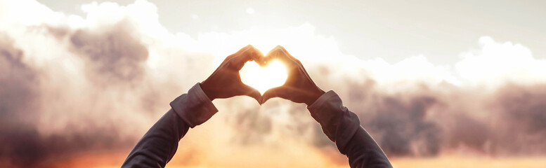 Female hands make heart shape on sunset sky background - Love, peace, protection, healthcare and...