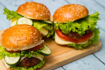 Burgers with beef meat, cheese and lettuce, served on cutting board