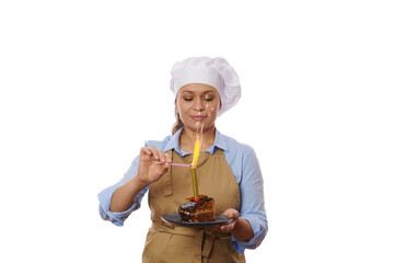 Multi-ethnic pretty woman, baker confectioner wearing chef hat and beige apron, lights a candle with sparklers on birthday cake, isolated on white background. Copy space. Anniversary. Baking concept