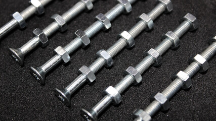 Metallic Nuts Are Evenly Screwed Onto Long Threaded Bolts In A Rows On A Black Surface  
