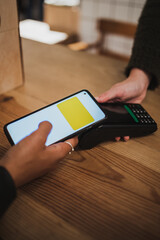 Close up shot of girls hand paying with her mobile phone using NFC on a POS in a shop.