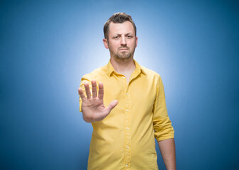 Man gesturing stop sign with palm of hand, refuses or reject something over blue background,...