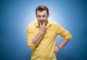Suspect concept. Distrustful young man staring to you over blue background, dresses in yellow shirt