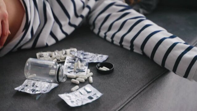 Woman committed a suicide by drug overdose lies on couch at home near empty blister packs and handful of pills. Unconscious depressed girl lying on a sofa after overdosing antidepressant medicine.