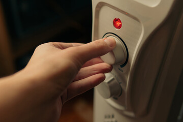 Man setting temperature on the oil electric heater on at home. Cold winter, economic crisis concept.