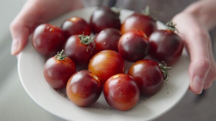 Retail and business, ripe black tomatoes on a plate in the hands of a woman.