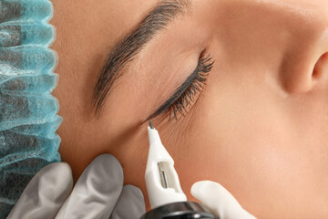 Young woman undergoing procedure of permanent eyeliner makeup, closeup - obrazy, fototapety, plakaty