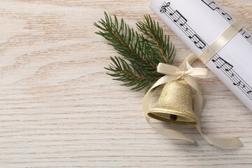 Golden shiny bell with bow, music sheet and fir twig on wooden table, flat lay. Space for text. Christmas decoration
