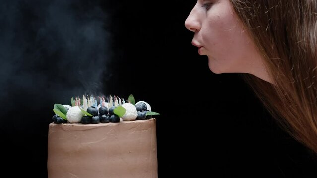 Chocolate cake with blueberries, and lighted candles. The girl blows out the candles, on a black background close-up, slow motion.