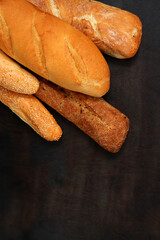 Bread on the table, top view. Long loaf, baguettes and buns with sesame seeds on a dark background