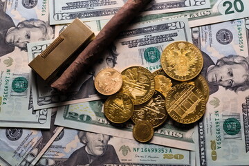 Golden coins on a background of 20 dollar bills with a Cuban cigar and vintage golden lighter