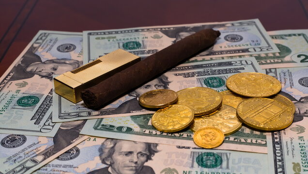Golden coins on a background of 20 dollar bills with a Cuban cigar and vintage golden lighter