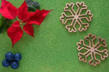 Christmas border with red poinsettia flowers in corner and two large wooden snowflakes, blue festive balls on green glitter paper, copy space for text.