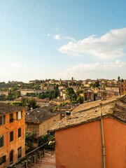 Obraz premium View of the city at sunset: you can see houses with yellow and orange stucco, roofs, and treetops.