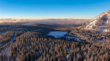 Aerial view of sunrise in the snow covered mountains with Lake Tahoe in the distant background.