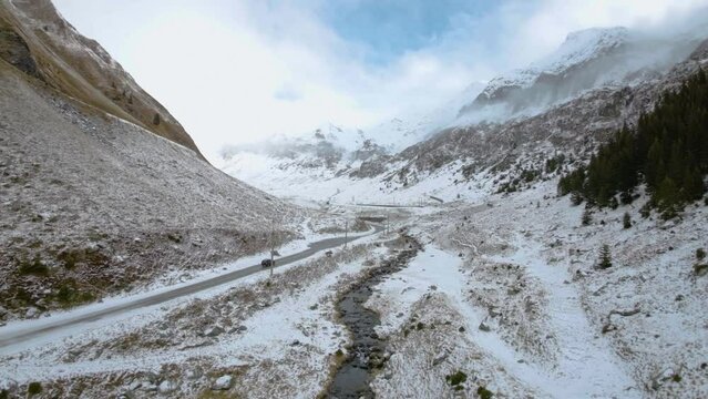 FPV Aerial view of car driving down on a frozen mountain road covered with snow. High altitude road. Highway on the mountain. Frozen mountain road in winter season. Winding road closed. Mountain fores