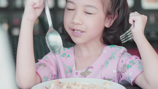 Face Close up of adorable asian girl kid who is hungrily eating macaroni with fork and spoon on table for her breakfast shows concept of delicious meal with healthy food for children.