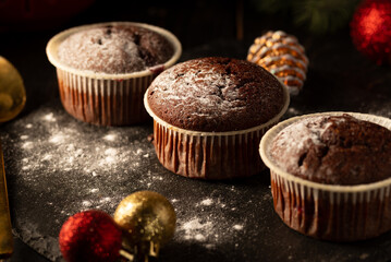 Chocolate muffins with powdered sugar on top on a black background. Christmas decoration . Still life close up. Food photo.