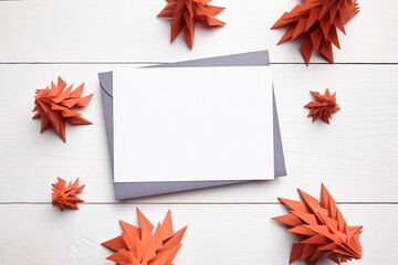Christmas card mockup with envelope and red paper fir trees on white wooden background, top view, flat lay