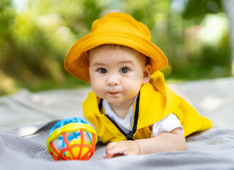 Little baby boy playing colorful toy on a blanket in the park looking to camera, close up. Outdoor fun for children.