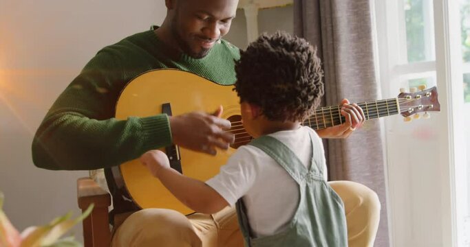 Animation of light flashing over happy african american father and son playing guitar