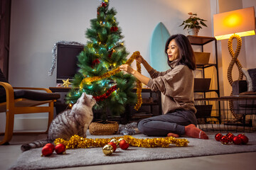 Beautiful Asian girl decorating Christmas tree in her livingroom