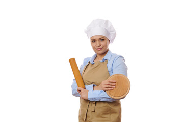 Confident female pastry chef portrait in professional uniform posing with wooden cutting board and rolling pin, over white background with free advertising space. Baking. Culinary master class concept