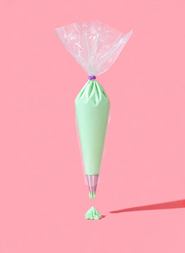 Frosting bag isolated on a pink background. Green buttercream icing in a plastic bag